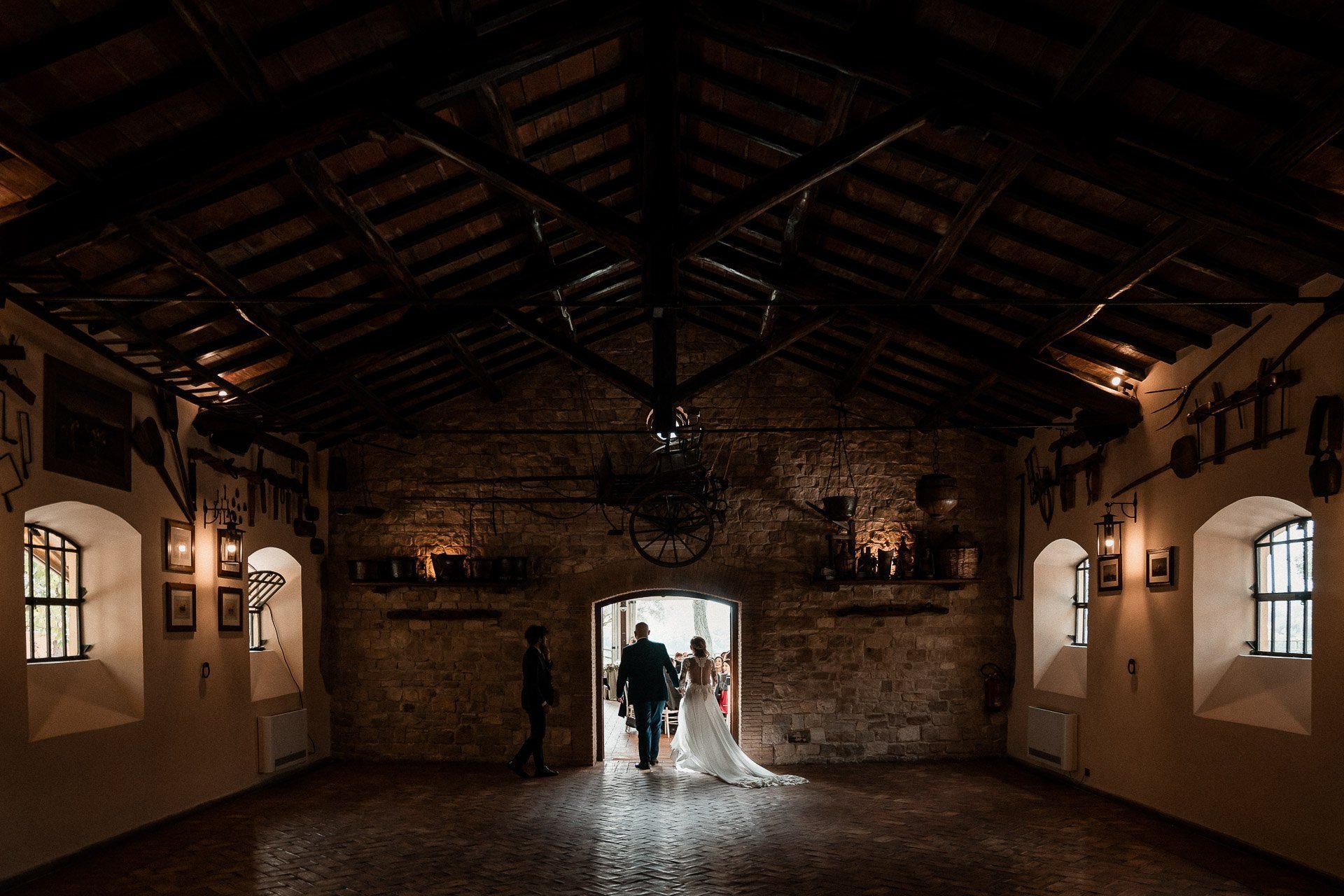 Coppia in abito da sposa esce da un edificio in pietra. Interni rustici e scarsa illuminazione.