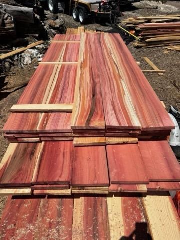 A stack of freshly milled cedar boards with vibrant red and cream-colored wood grain, outdoors at a lumber yard.