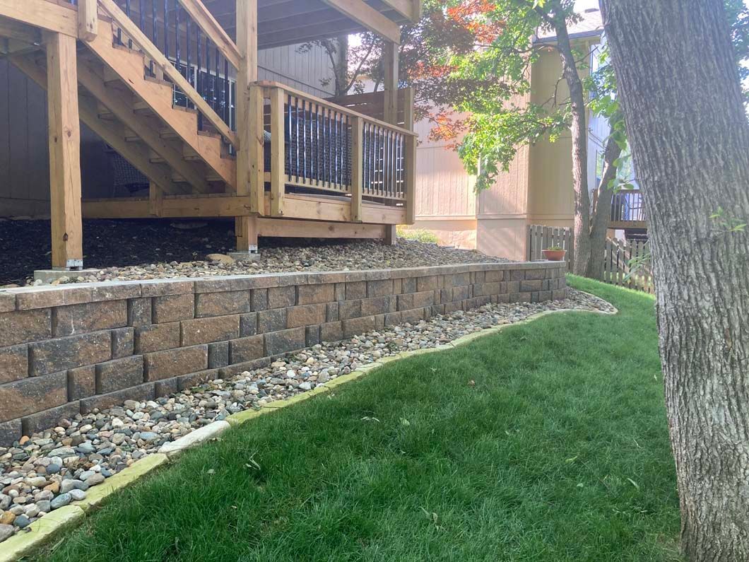 A stone wall surrounds a lush green lawn in front of a house.