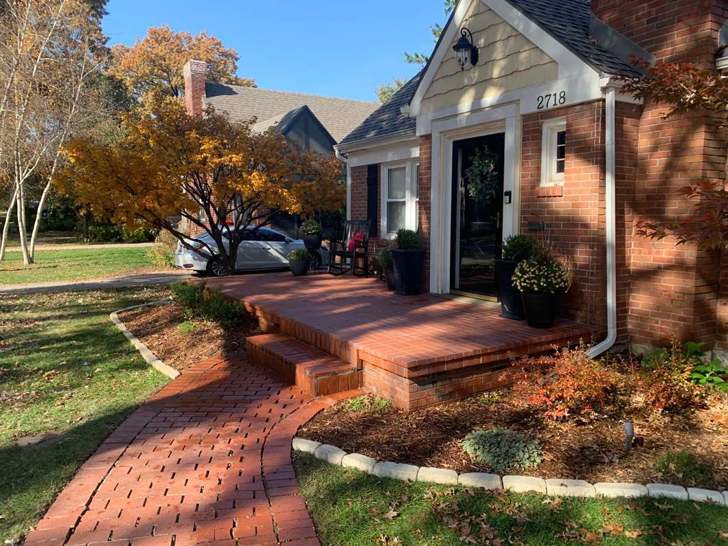 A brick walkway leading to a brick house with a car parked in front of it.