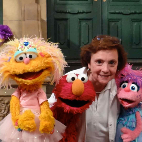 Woman poses with Elmo and two other Sesame Street Muppets in front of a green door.