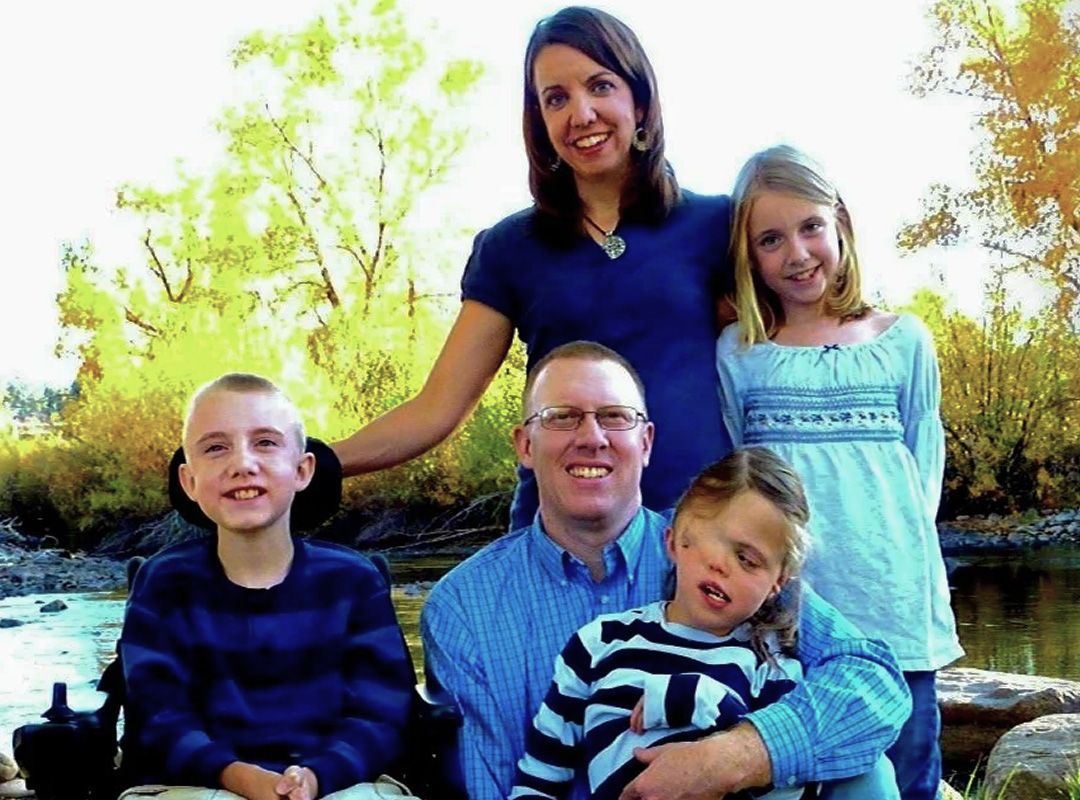 Family portrait in front of a river. Parents and three children, one in a wheelchair. Autumn trees in the background.