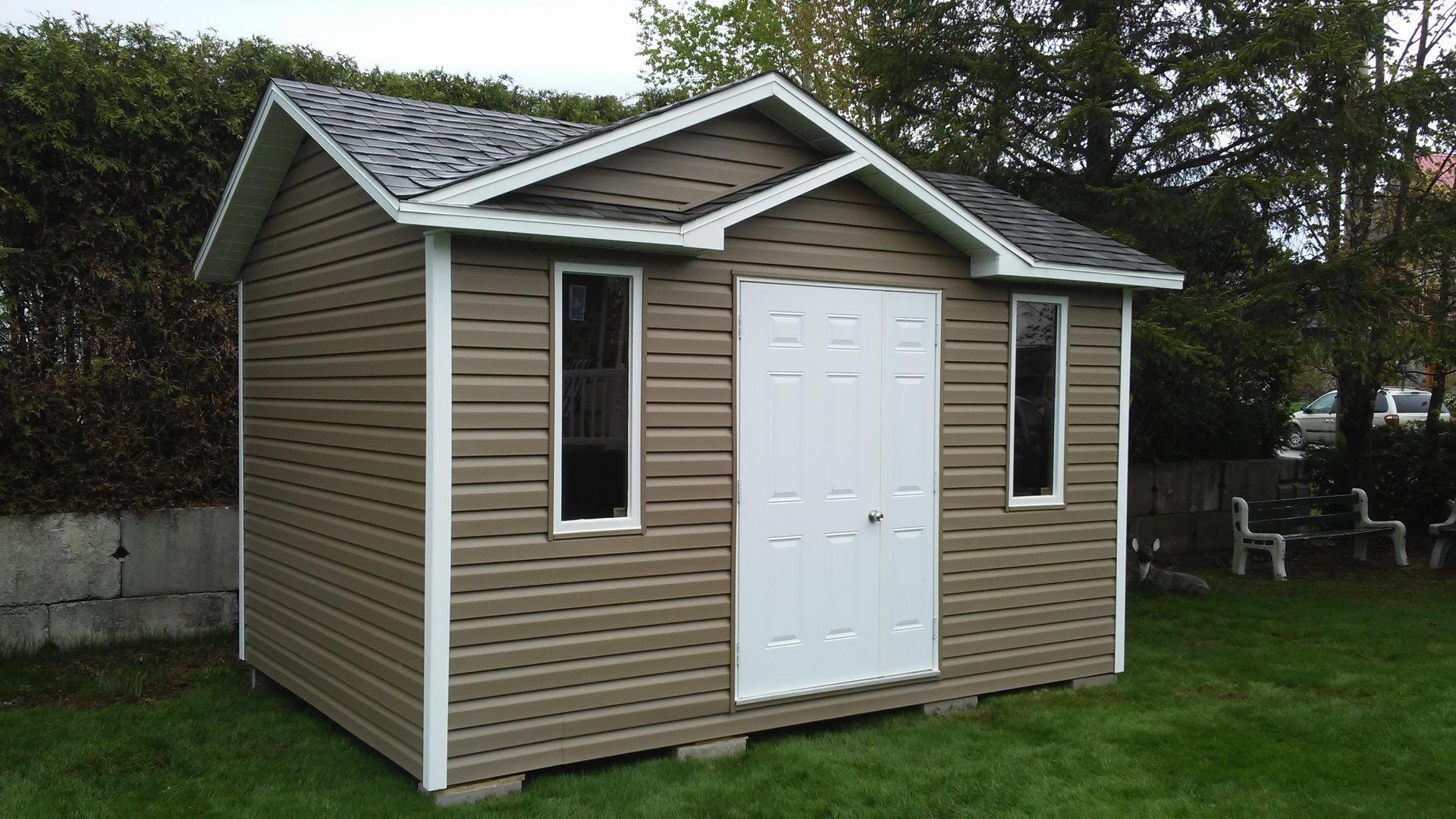 Cabanon marron et blanc sur une pelouse verte, avec une porte blanche et deux fenêtres.