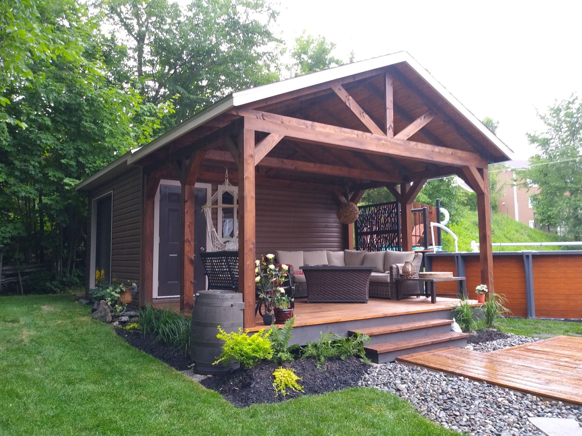 Chalet en bois avec véranda couverte, donnant sur une piscine et un jardin paysager.
