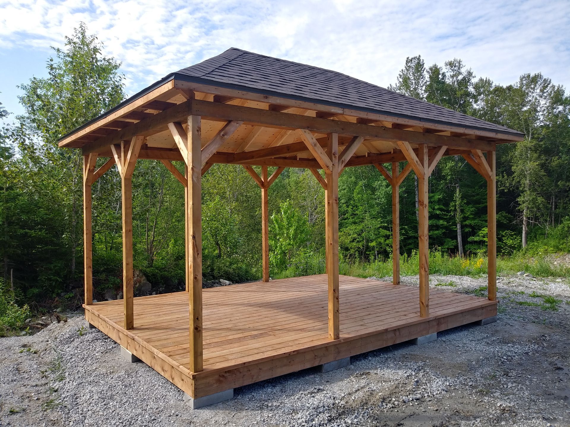 Gazebo en bois avec un toit en bardeaux foncés, installé sur une terrasse en bois dans un cadre naturel extérieur.