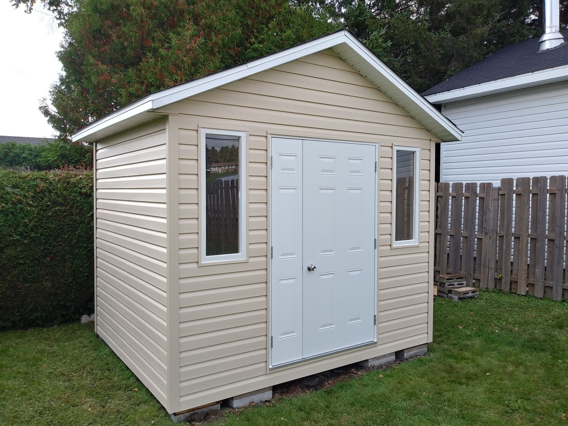 Abri beige avec porte et fenêtres grises sur pelouse verte.