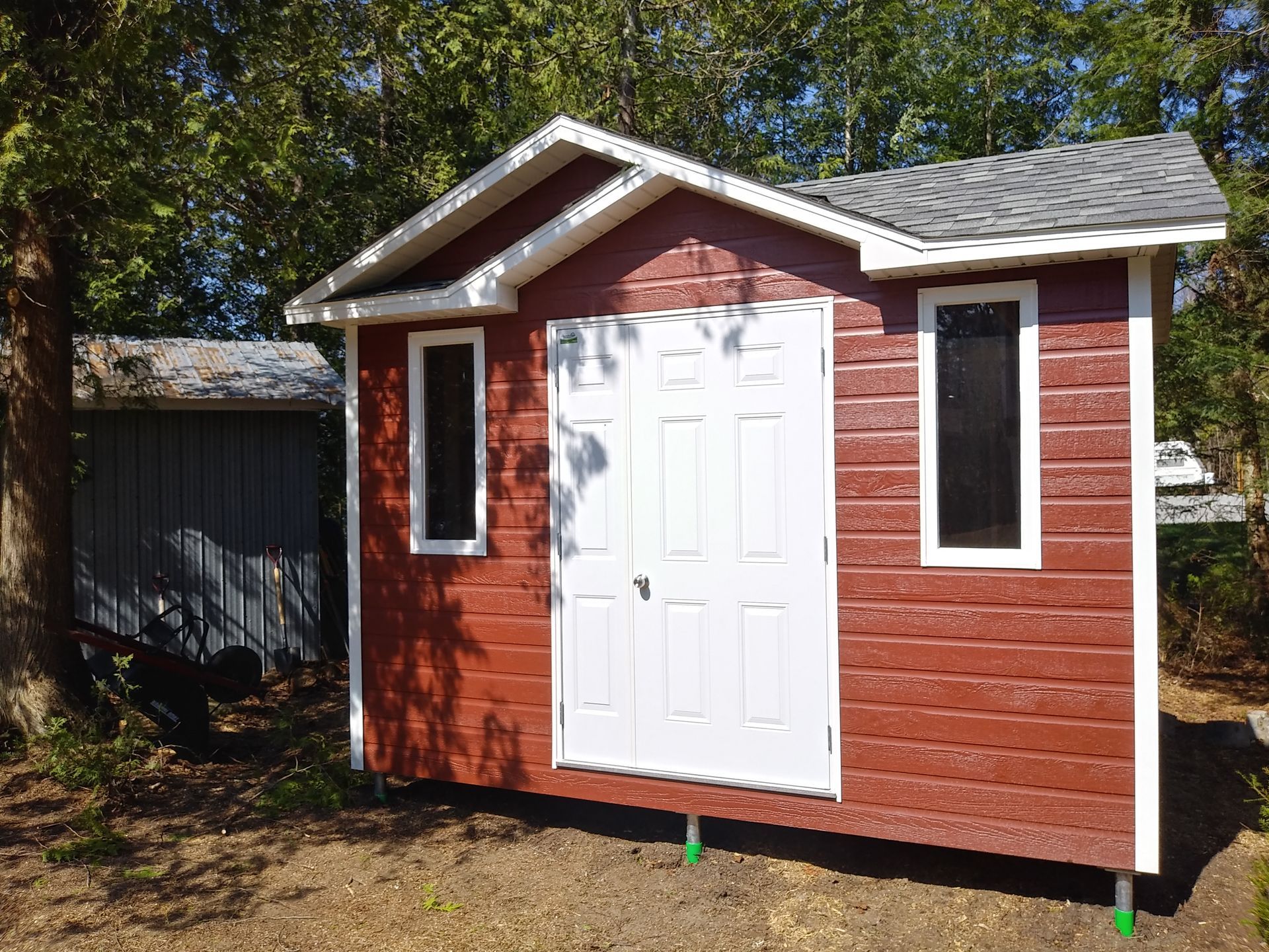 Abri de jardin rouge à bordures blanches, double porte et deux hautes fenêtres ; situé à l'extérieur, sur l'herbe.