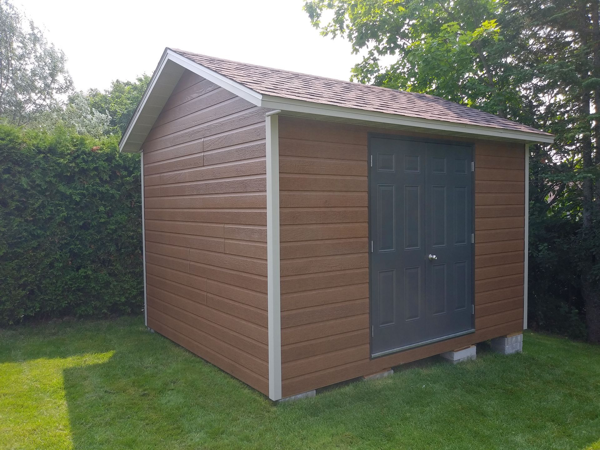 Abri marron avec porte et toit gris, sur une pelouse verte.