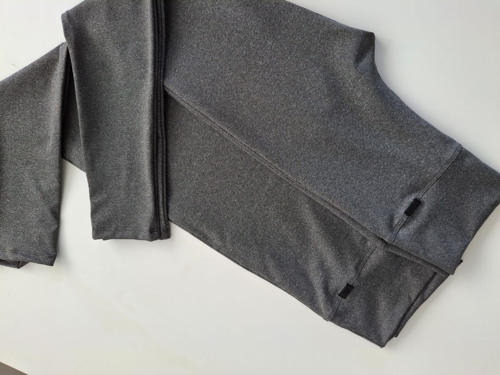 Mallas deportivas grises colgadas en una percha contra una pared de ladrillos blancos.