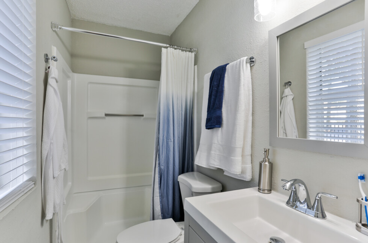 A bathroom with a toilet , sink , mirror and shower curtain.
