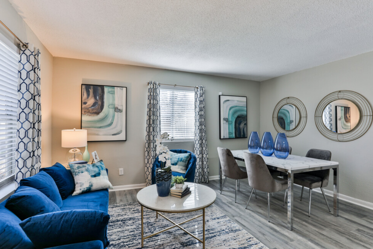 A living room with a blue couch , chairs , table and mirrors.