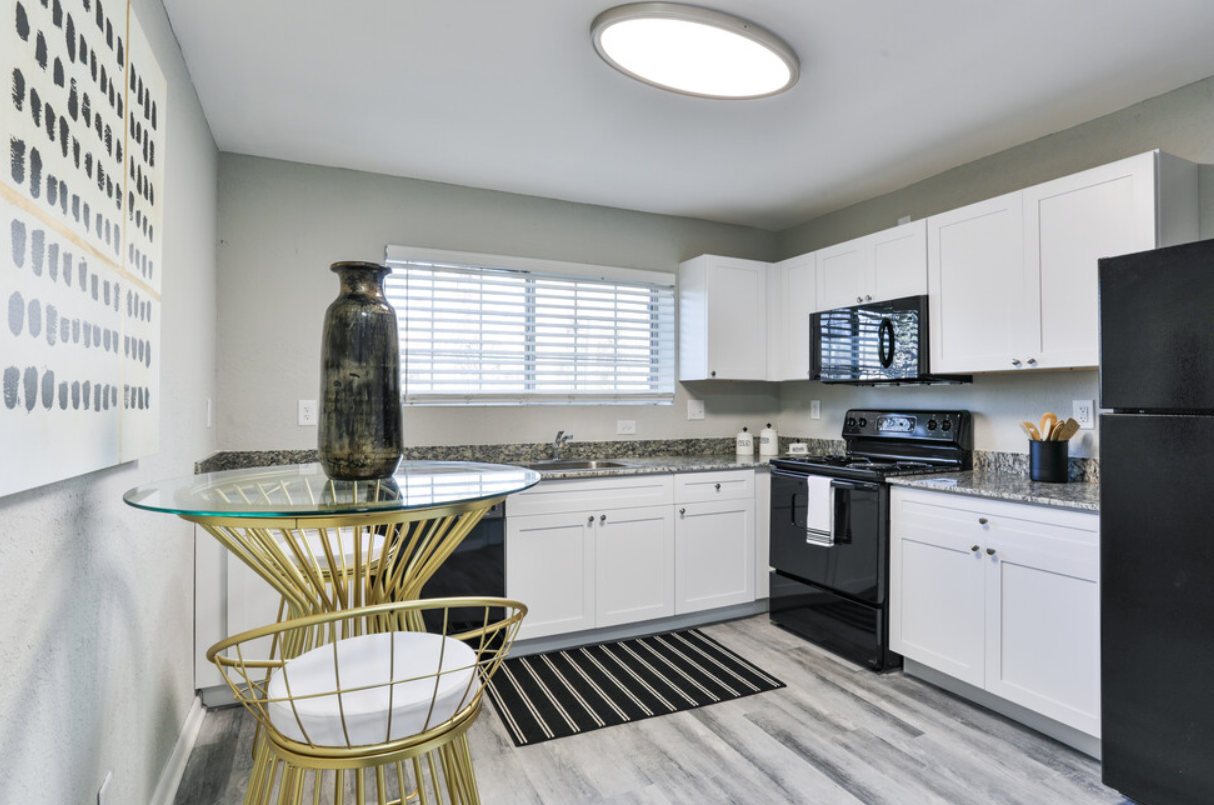 A kitchen with white cabinets , black appliances , a table and chairs.