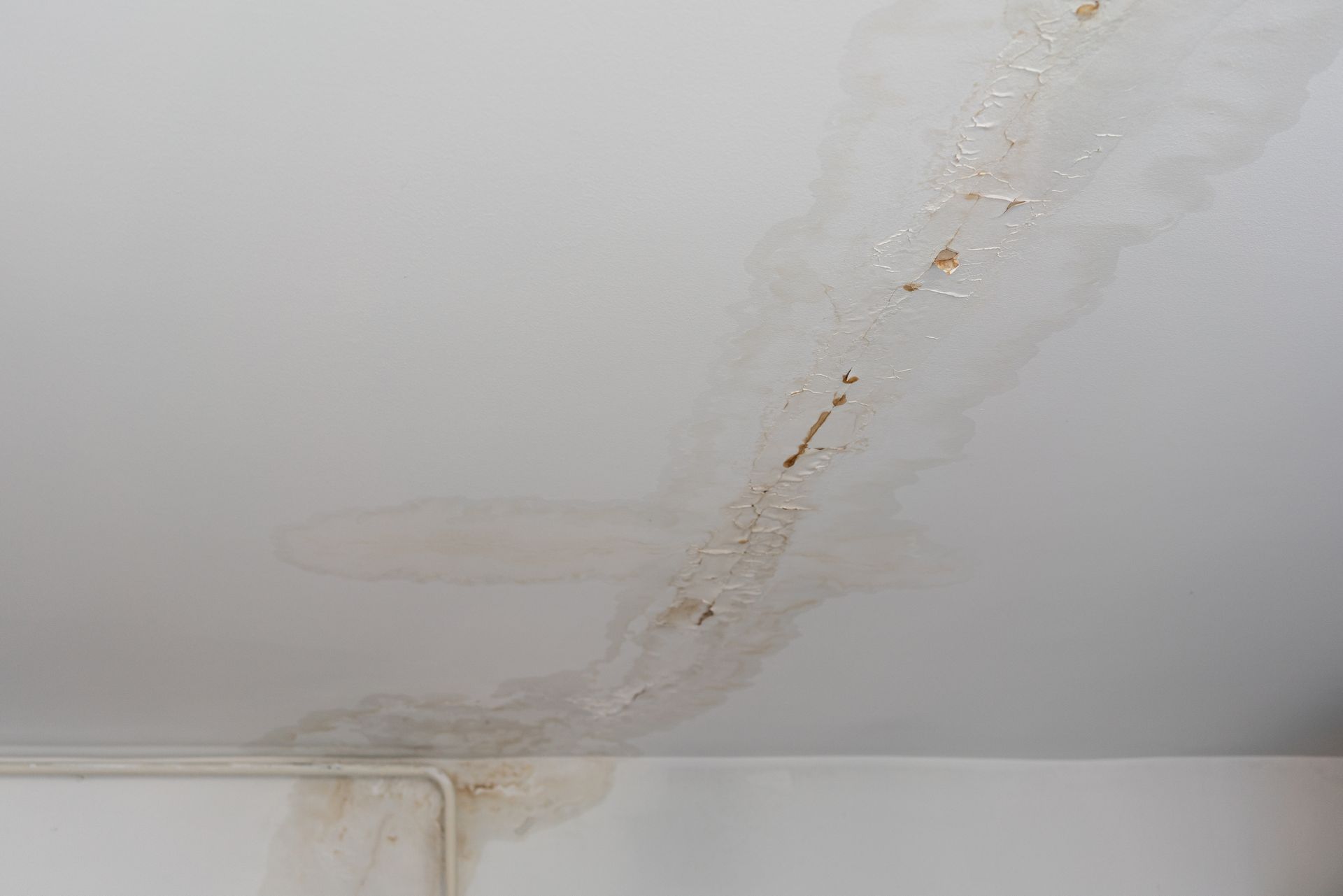 Water stain and peeling paint on white ceiling showing long-term leak damage along seam