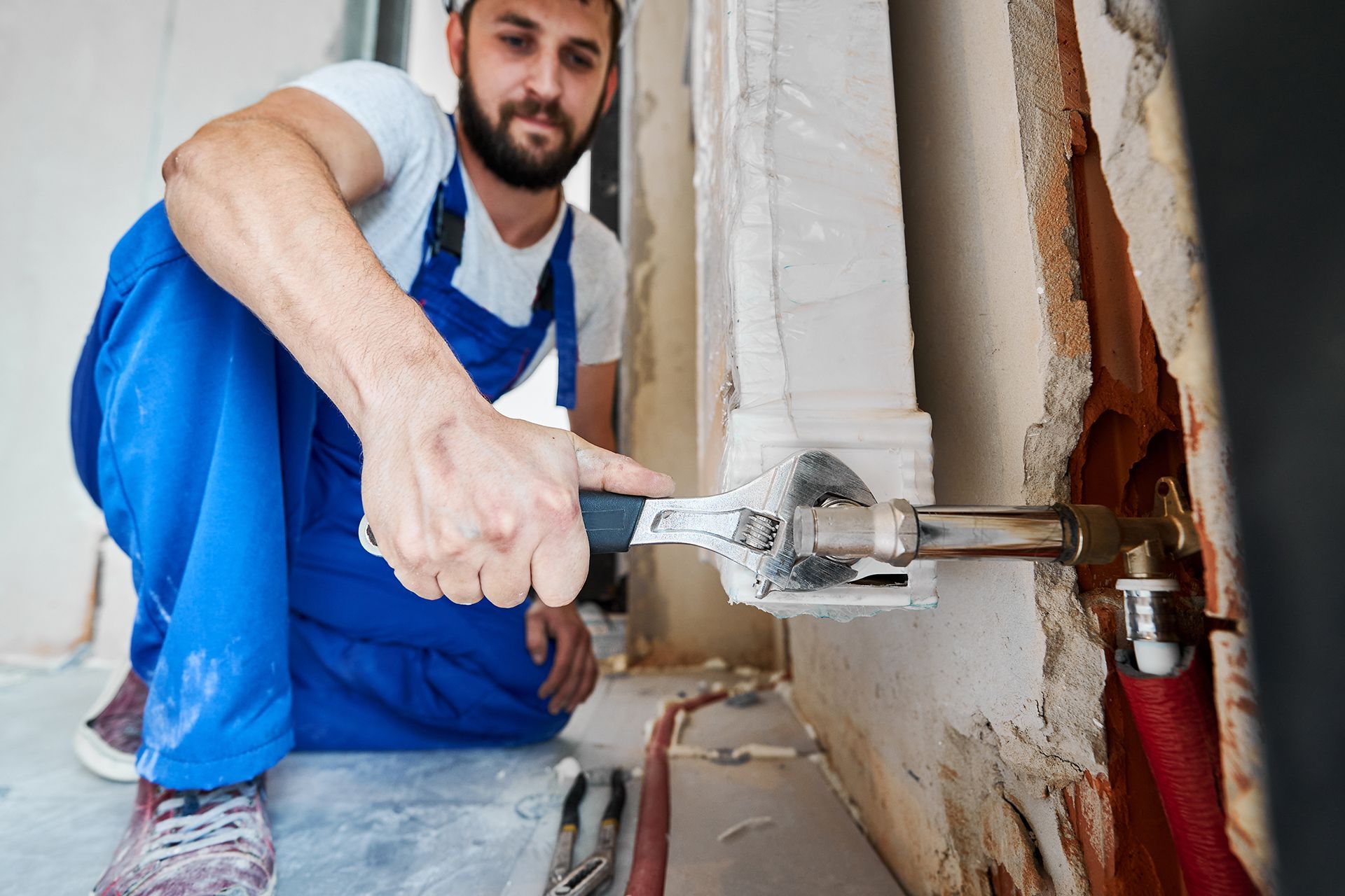 A plumber using a wrench is tightening an indoor water hose.