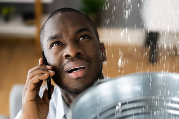 A man calling a plumber for an overhead burst pipe.