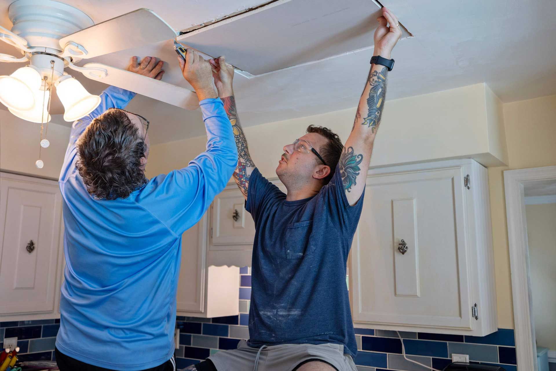 Two workers putting drywall on the ceiling to cover a hole from a water leak.