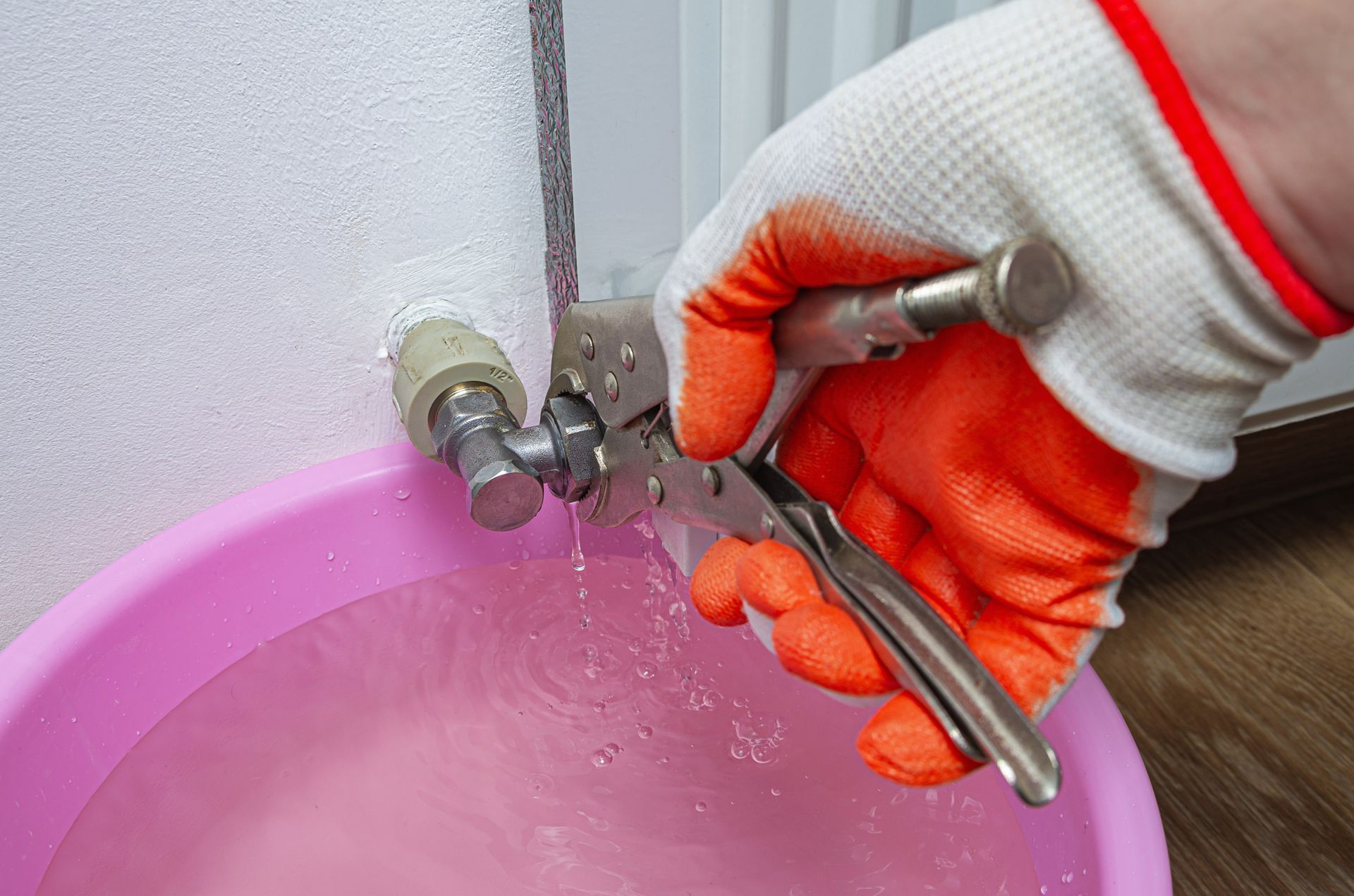 A plumber working on fixing a burst pipe with a bucket to catch the dripping water.