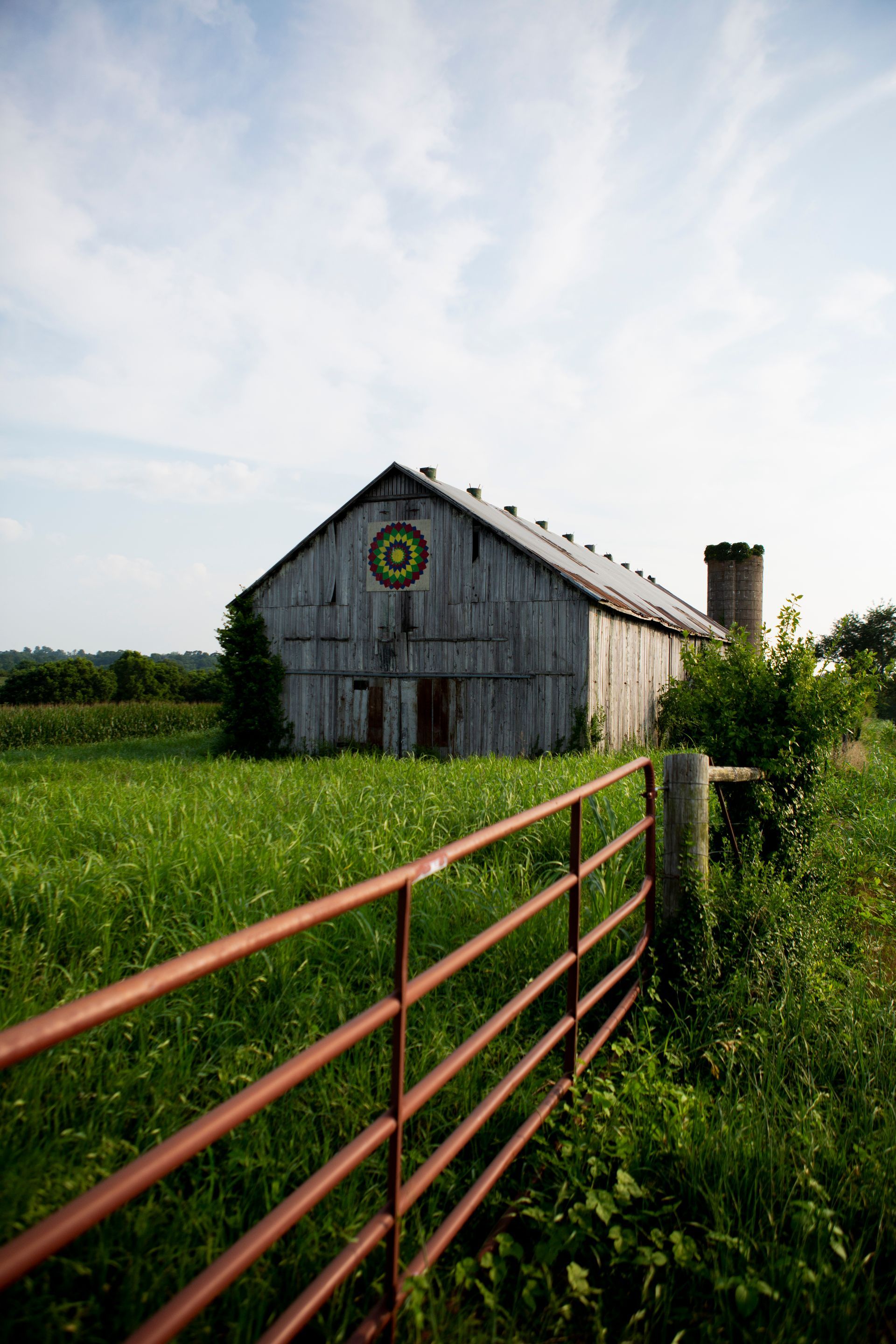 a barn is sitting in the middle of a grassy field next to a fence .