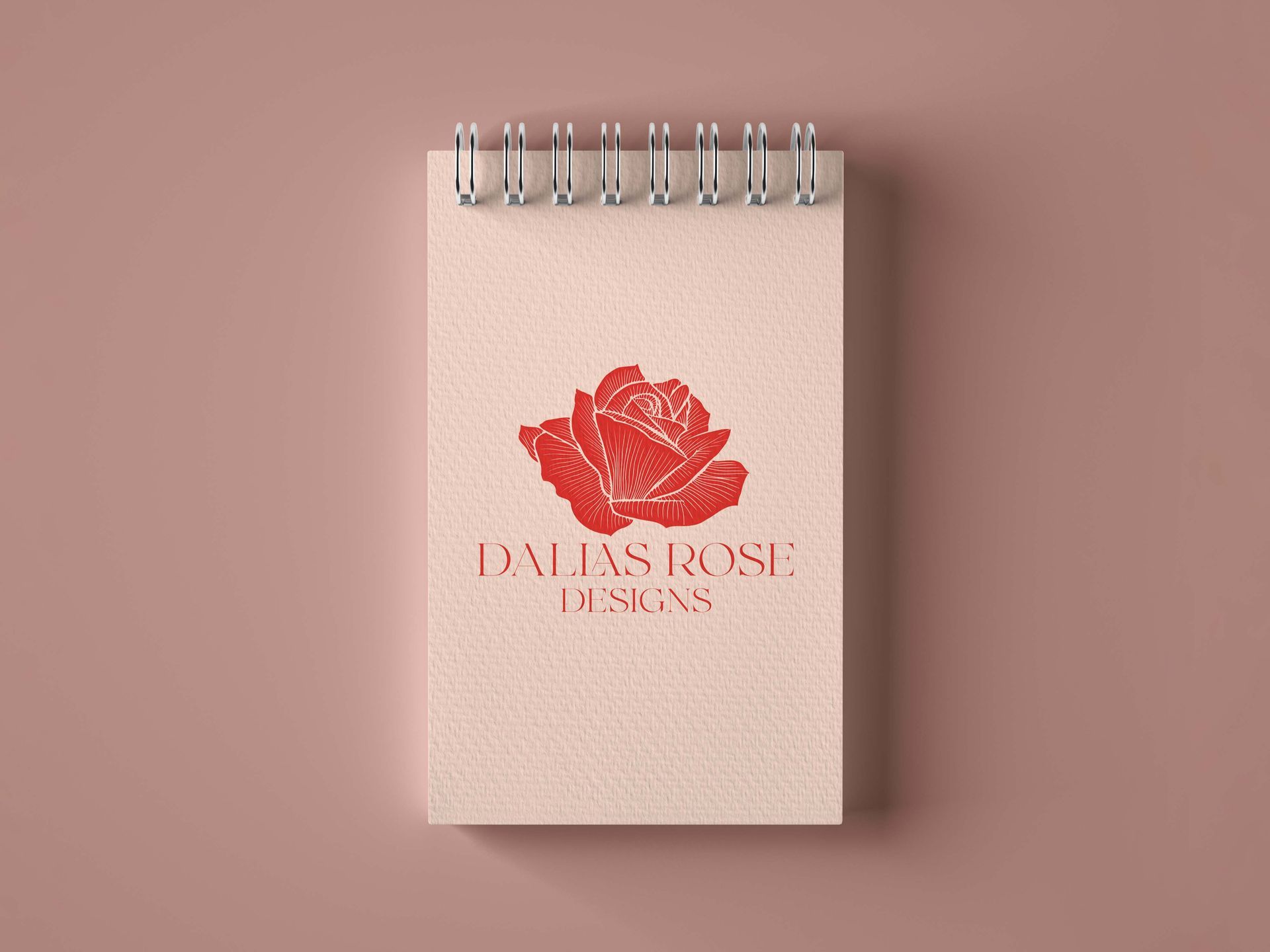 A notebook with a red rose on it is sitting on a pink surface.