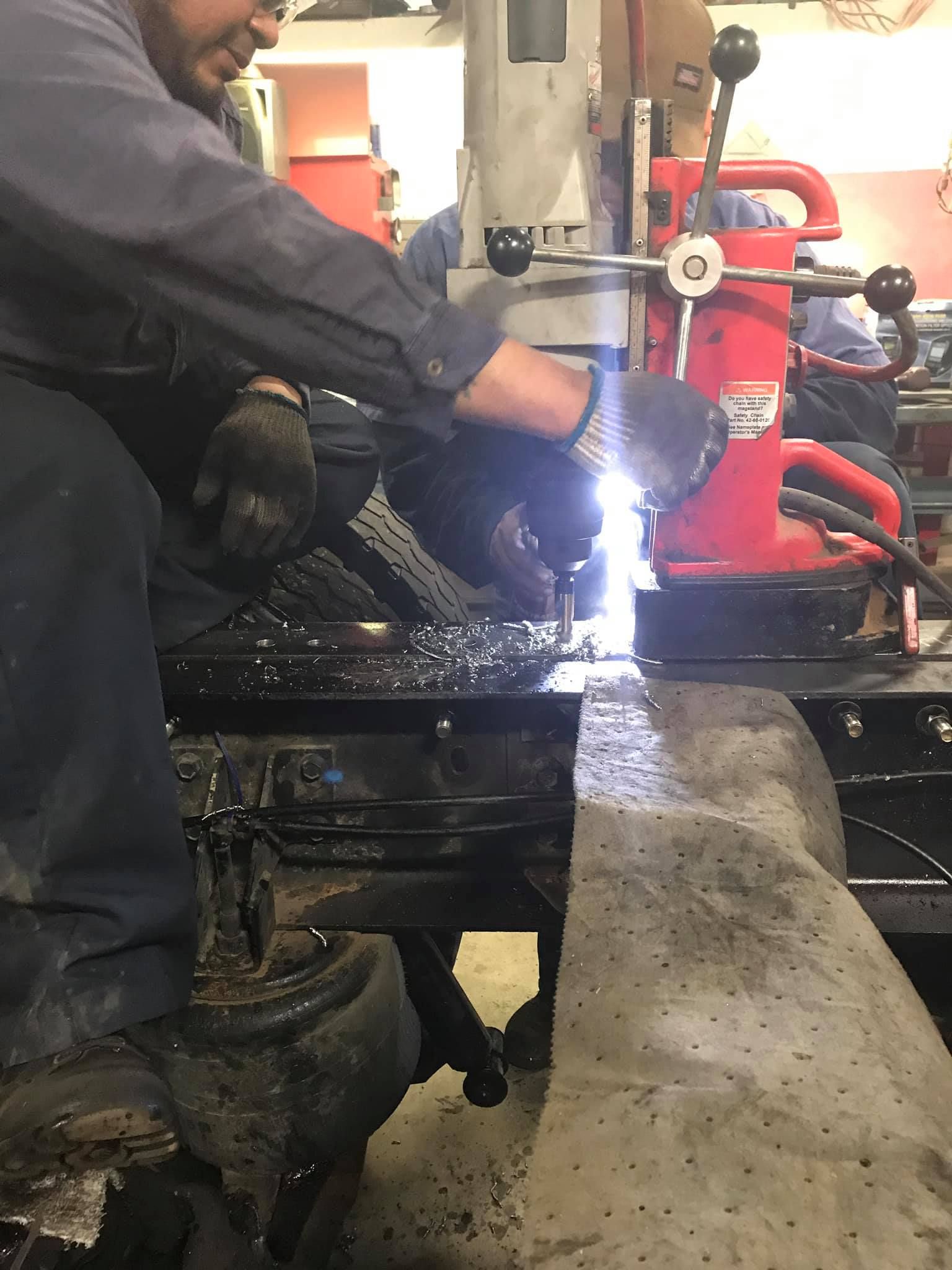 Man welding metal on a vehicle in a workshop, with a bright light and protective gloves.