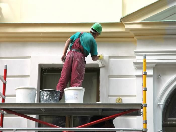A man is painting the side of a building on a scaffolding.