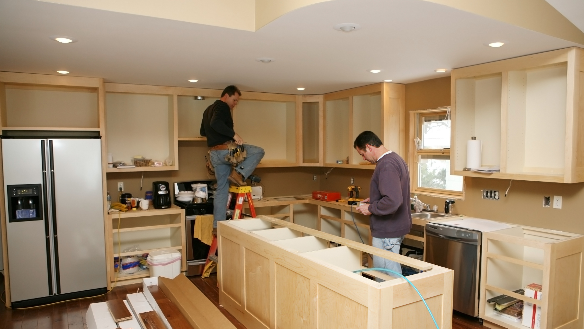 Two men are working in a kitchen with a stainless steel refrigerator