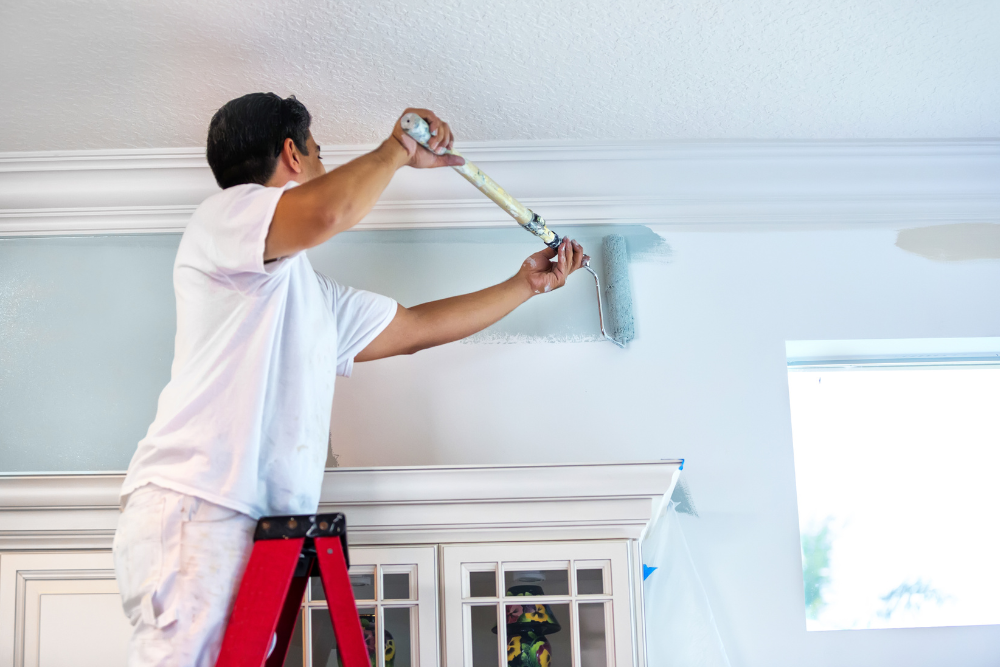 A man is standing on a ladder painting a wall.