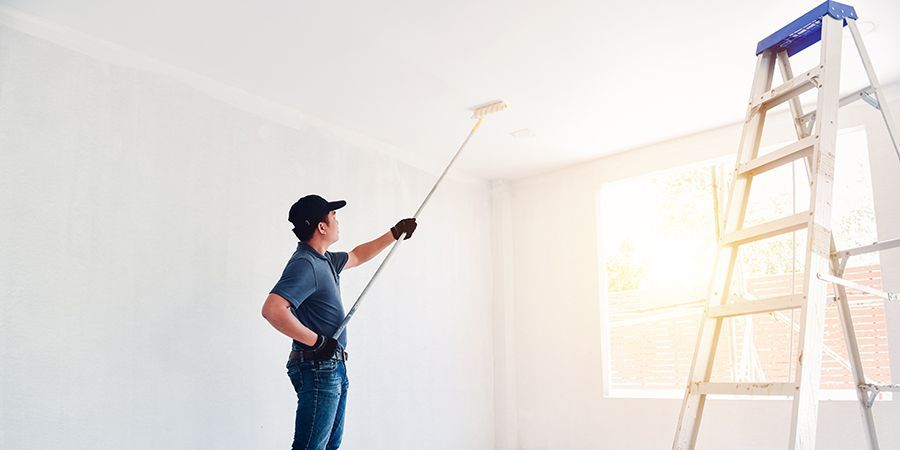 A man is painting the ceiling of a room with a paint roller.
