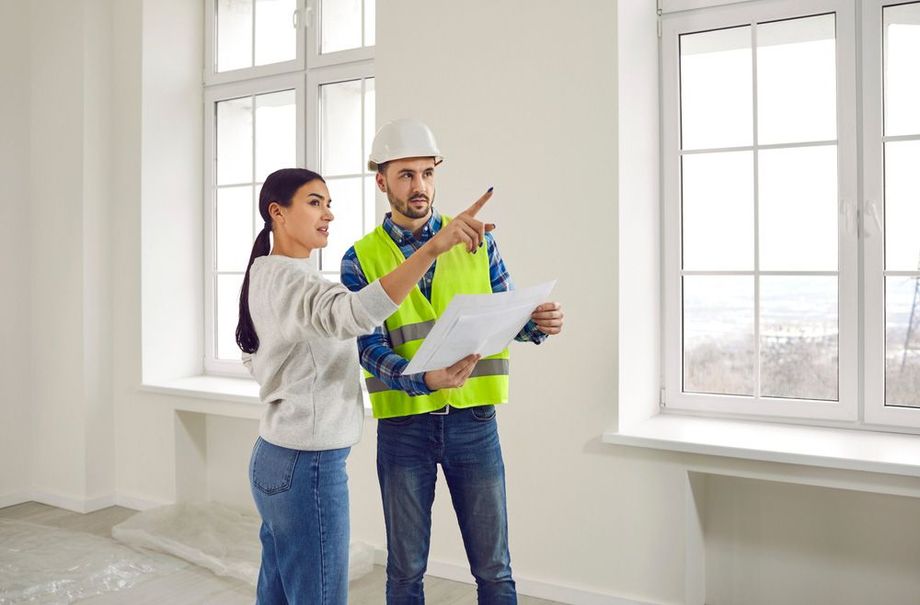 A man and a woman are looking at a blueprint in an empty room.