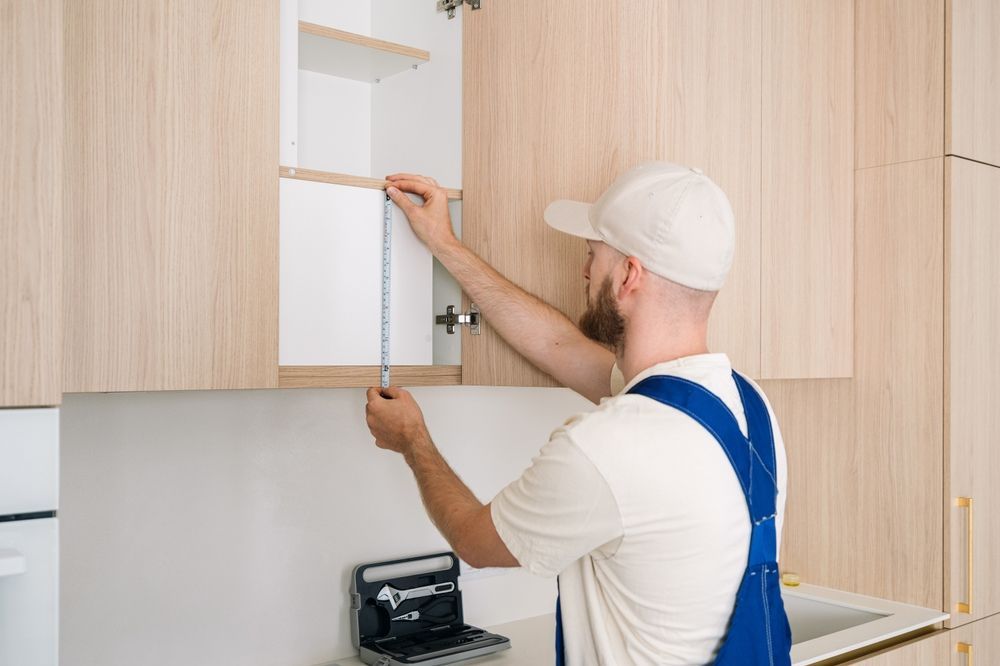 A man is measuring a cabinet with a tape measure in a kitchen.