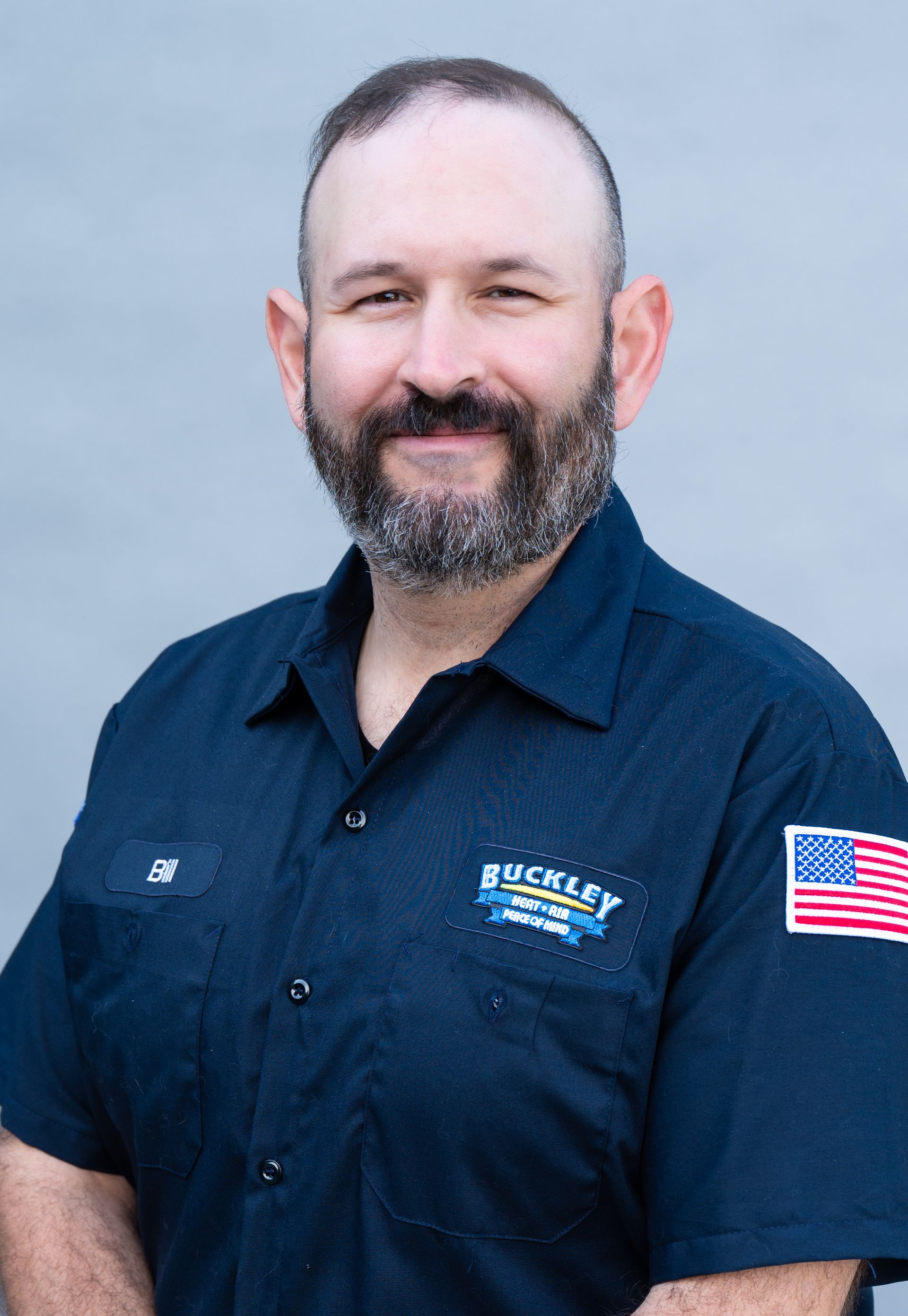 A man with a beard is wearing a blue shirt with an american flag on the sleeve.