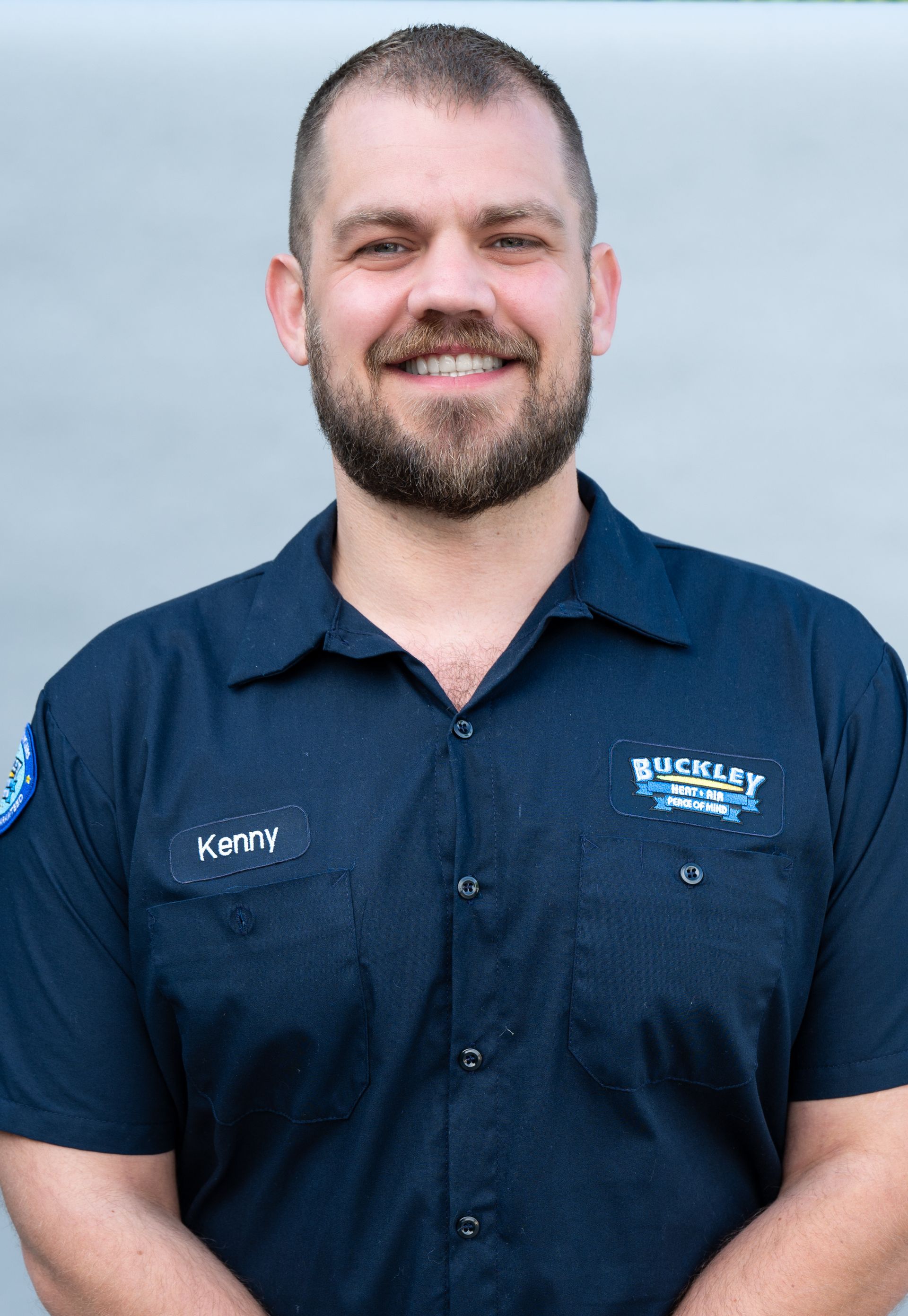 A man with a beard is wearing a blue shirt and smiling.