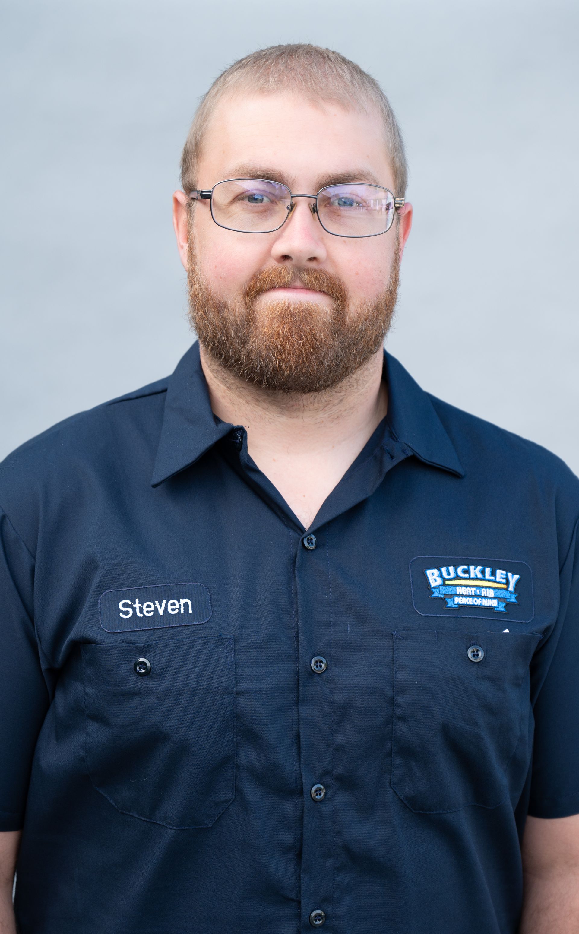 A man with a beard and glasses is wearing a blue shirt.