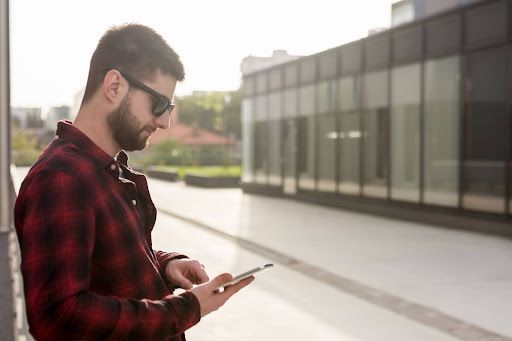 A man is standing on a sidewalk looking at his cell phone.