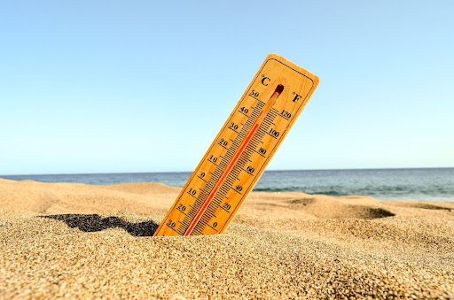 A thermometer is sticking out of the sand on a beach.