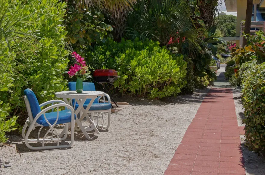 Garden path with white gravel, red brick walkway, and blue chairs beside lush greenery.