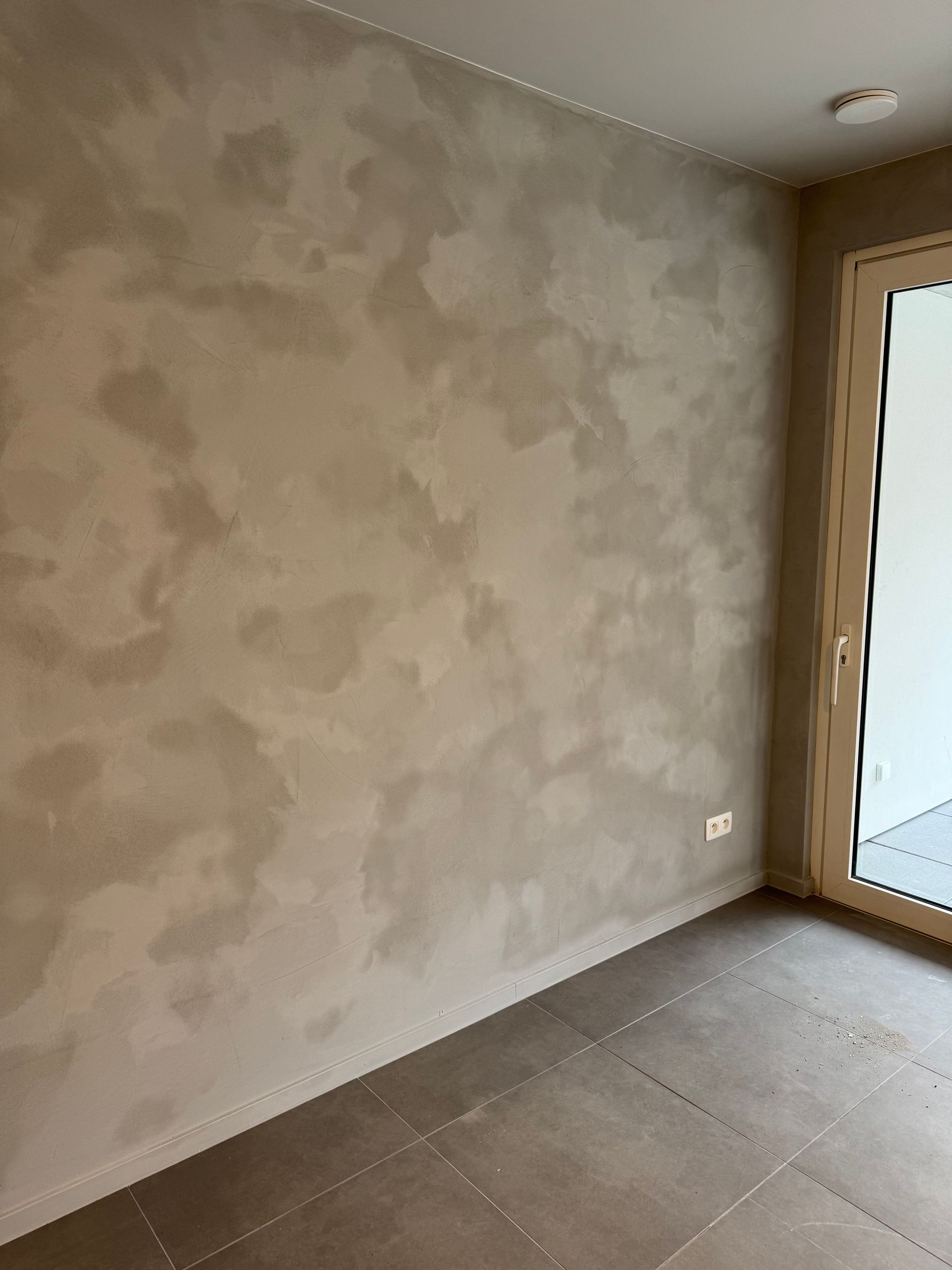 Een lege kamer met een glazen schuifdeur en een grijze muur.