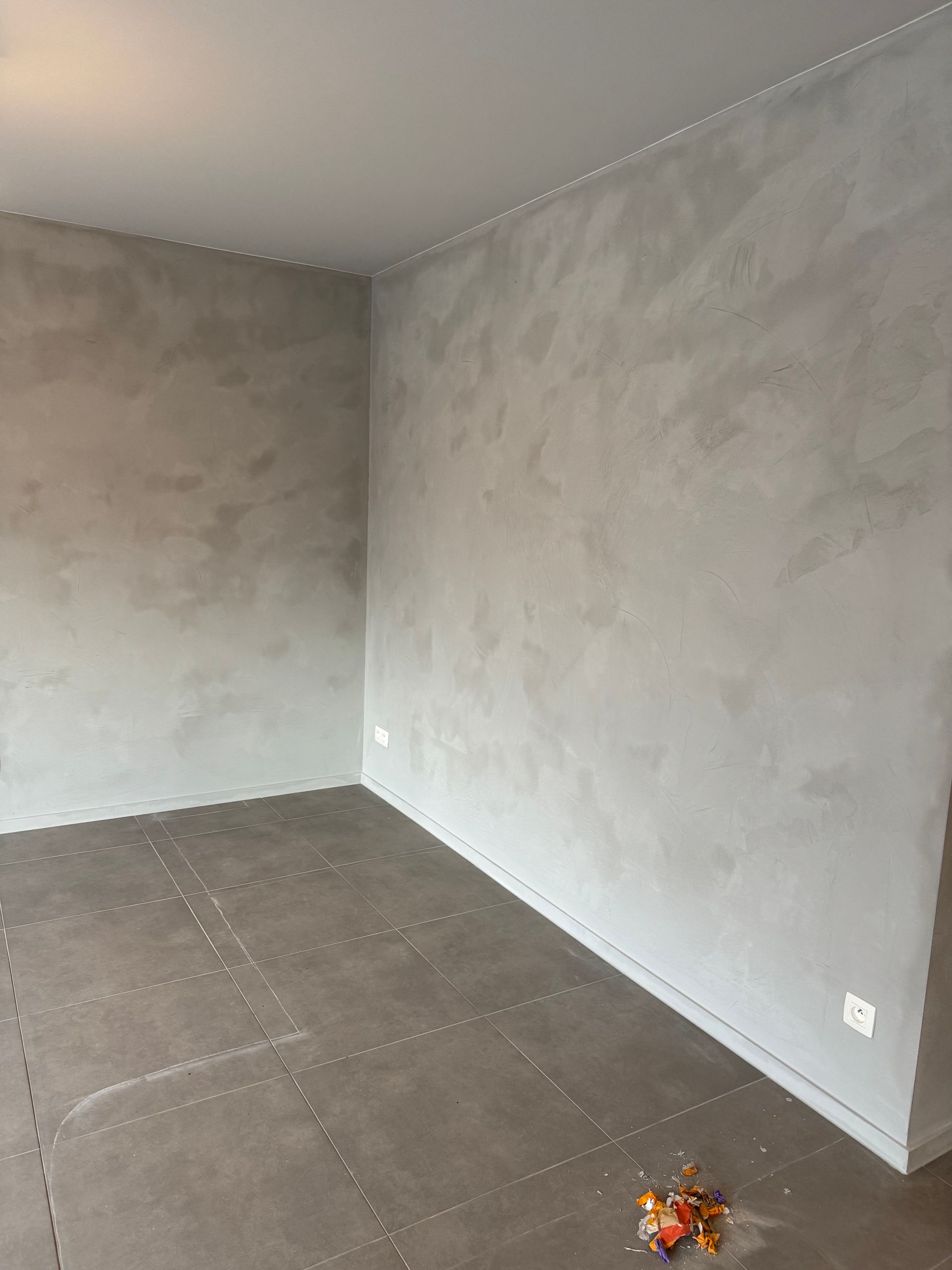 Een lege kamer met een grijze muur en een bruine vloer.