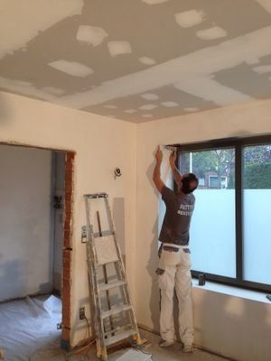 Een man staat in een kamer met een ladder voor een raam.