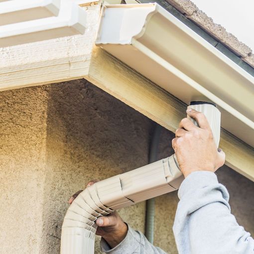 a man is installing a gutter on the side of a house .