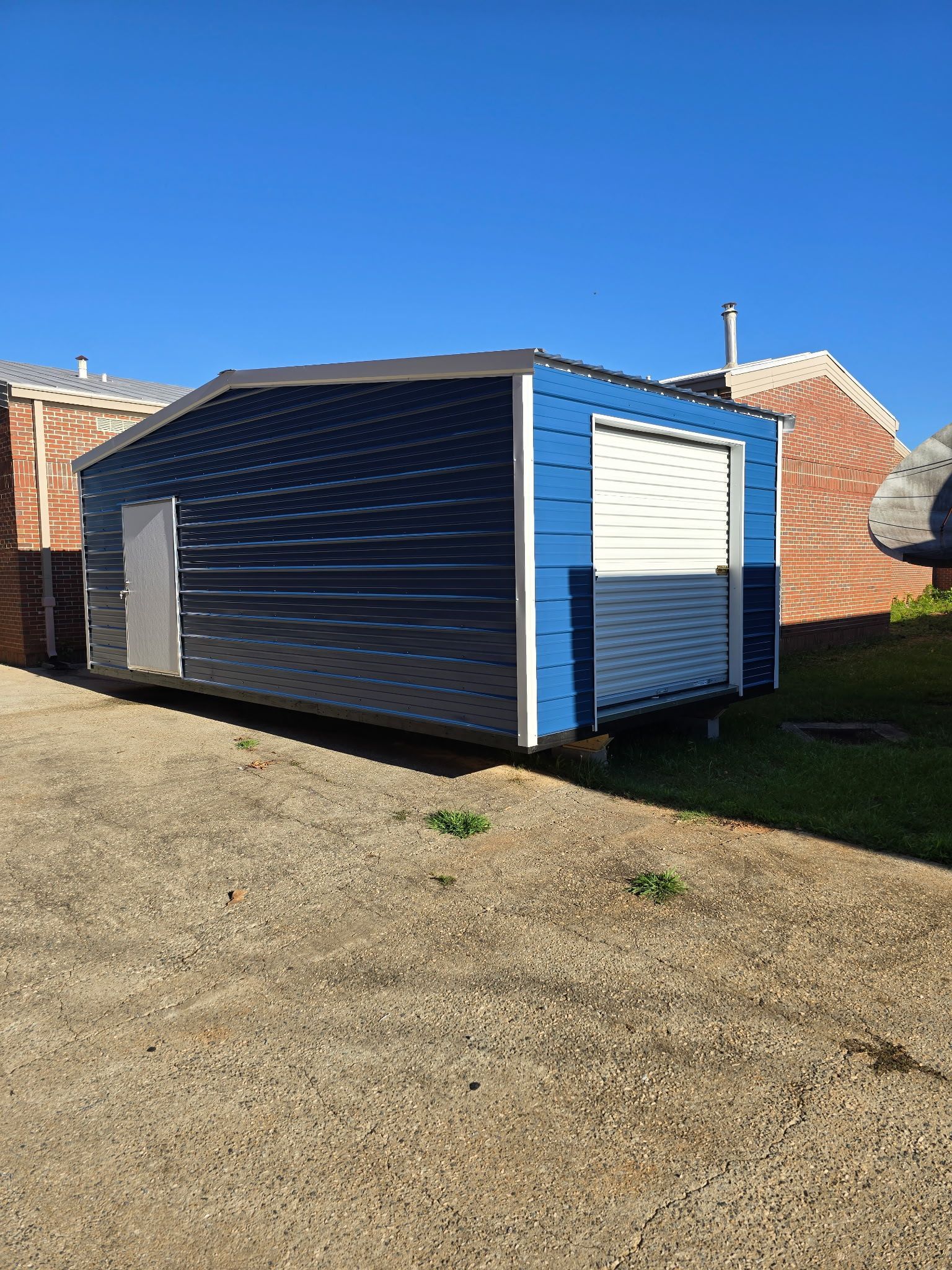 Blue-and-white shed on gravel beside brick buildings under a clear sky