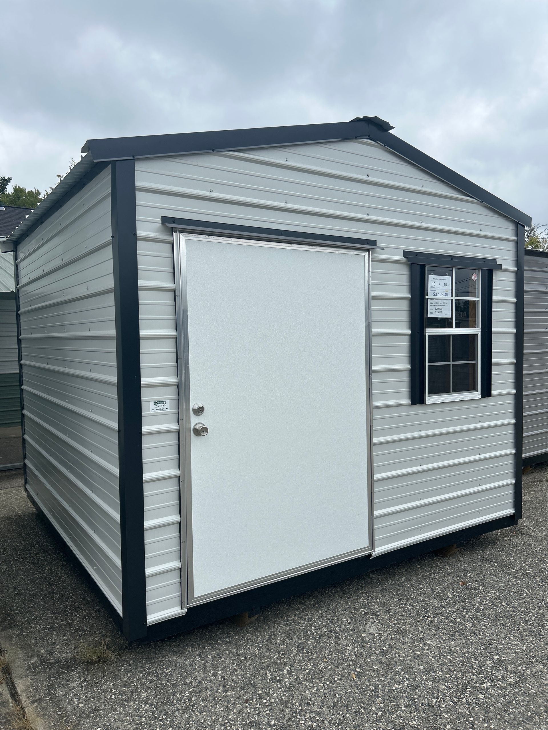 Gray metal shed with white door and window, black trim, overcast sky.