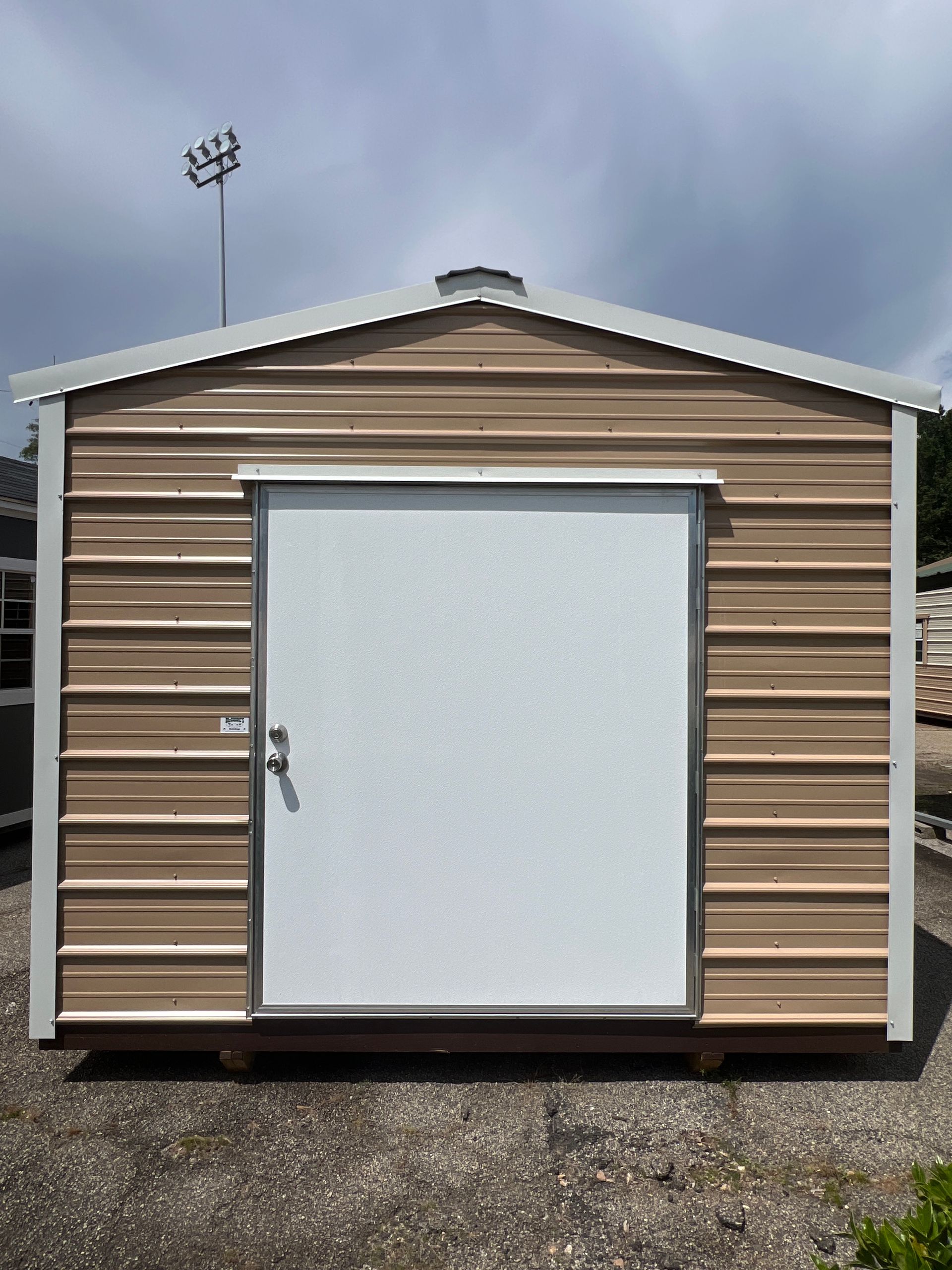 Tan metal shed with a white door, sitting outdoors.