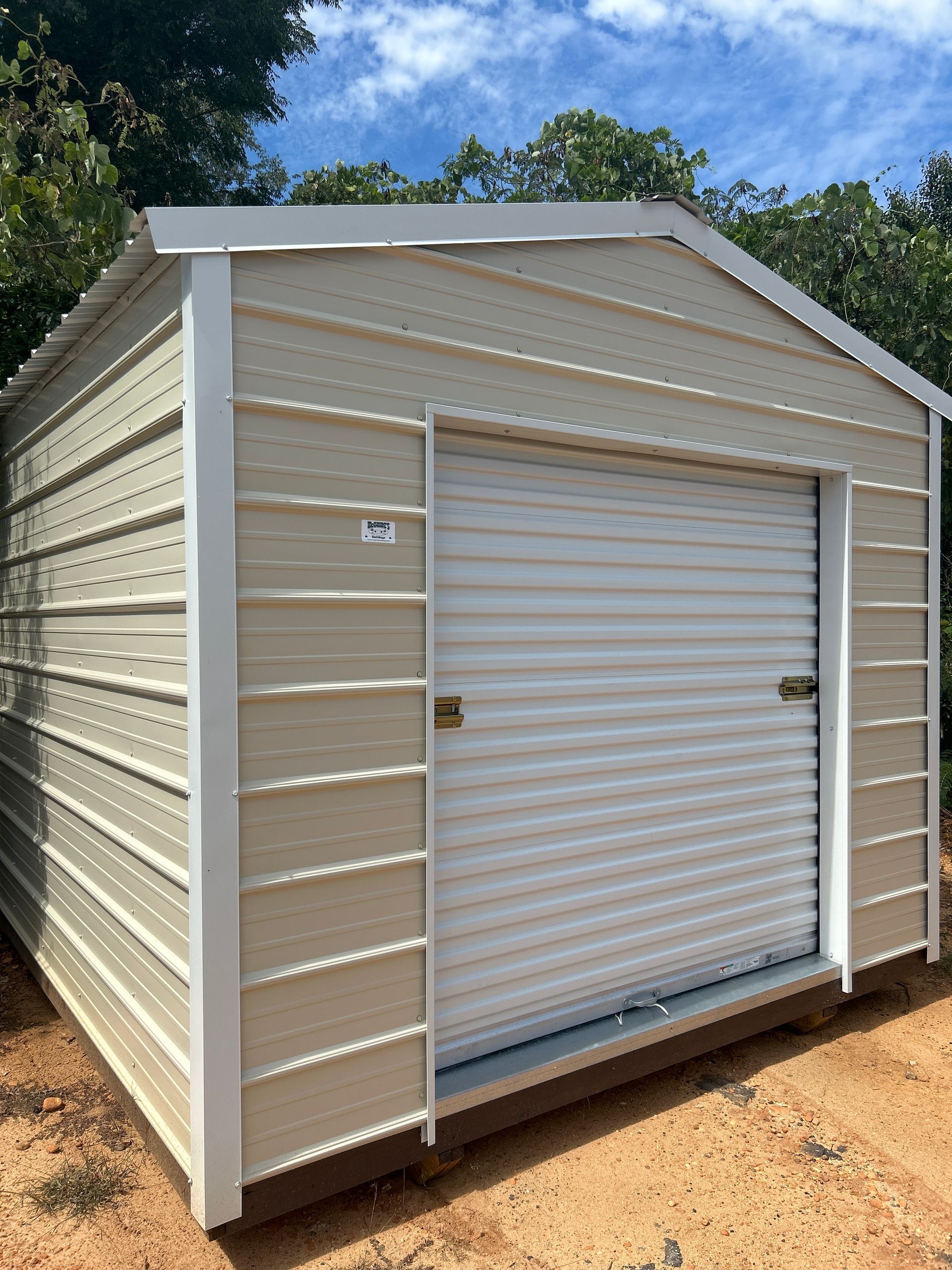 Tan metal shed with a roll-up door on a brown base, set against a blue sky.