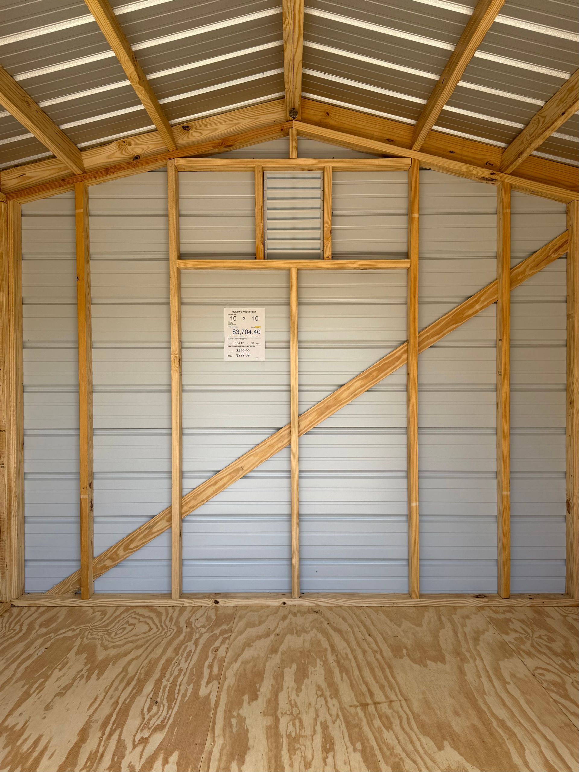 Interior of a wooden barn with corrugated metal walls and roof, showing diagonal braces and a dirt floor.