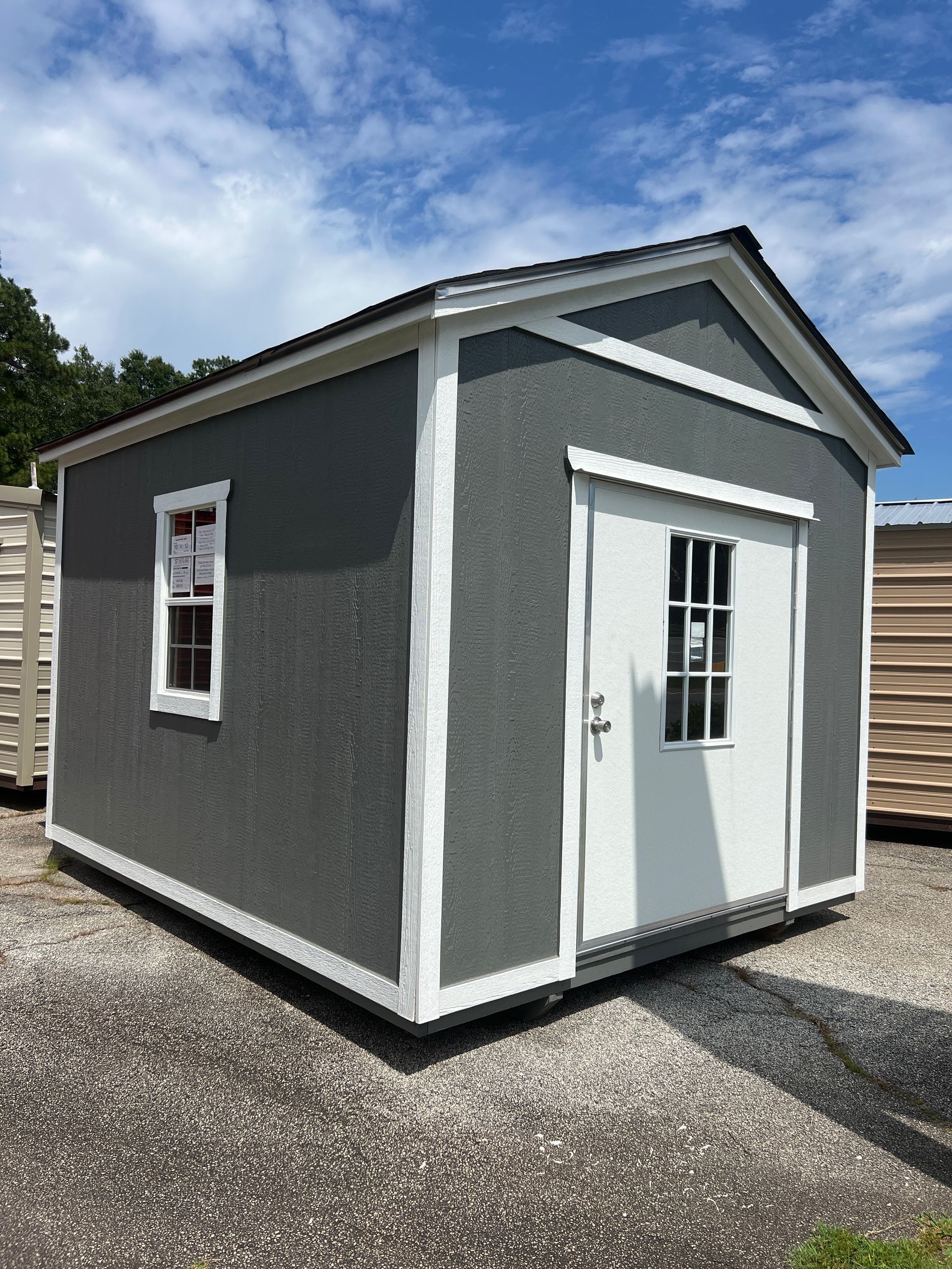 Gray shed with white trim, door, and window, under a blue sky with scattered clouds.