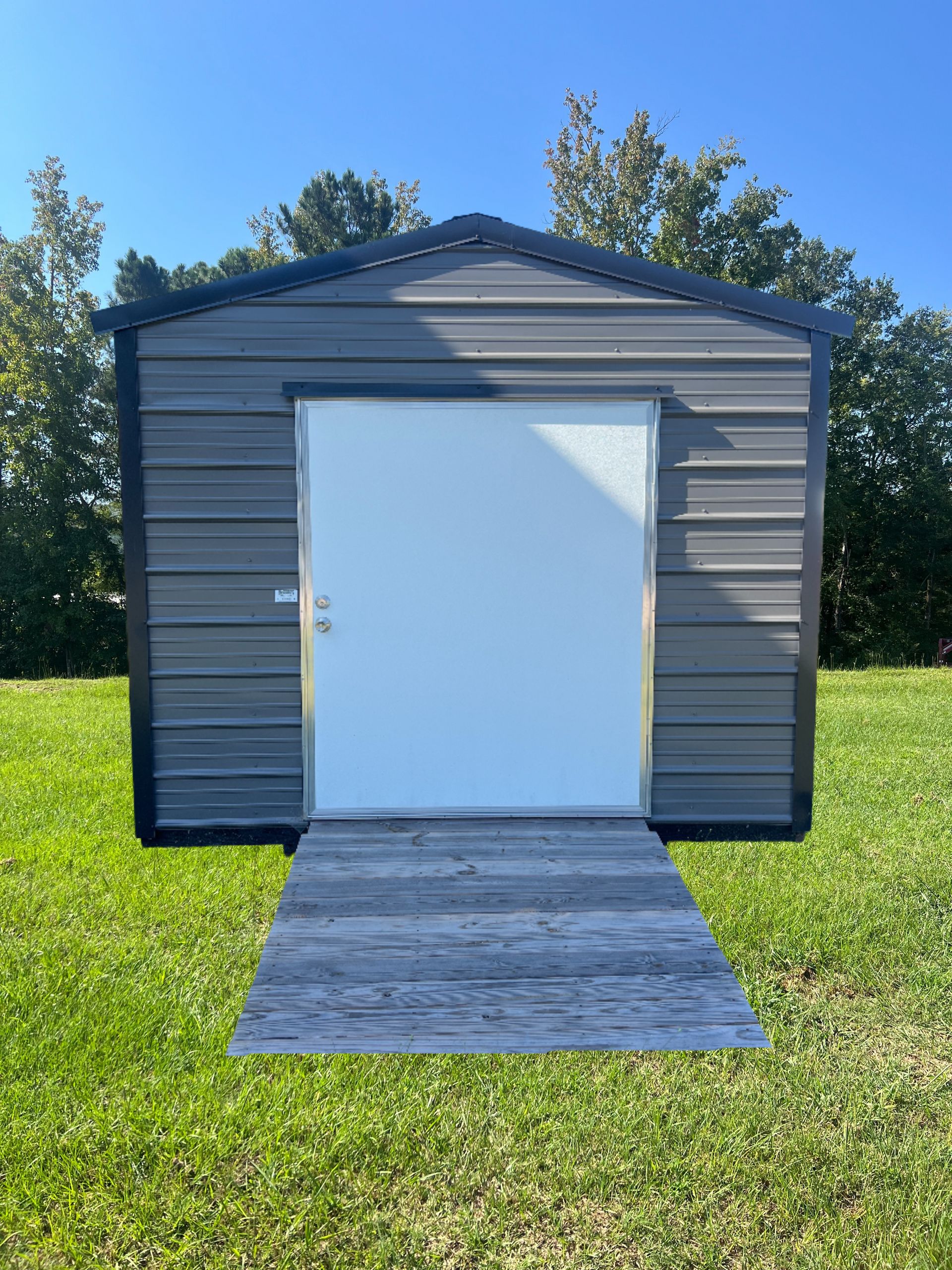 Metal shed with a white door, gray ramp, and green grass.