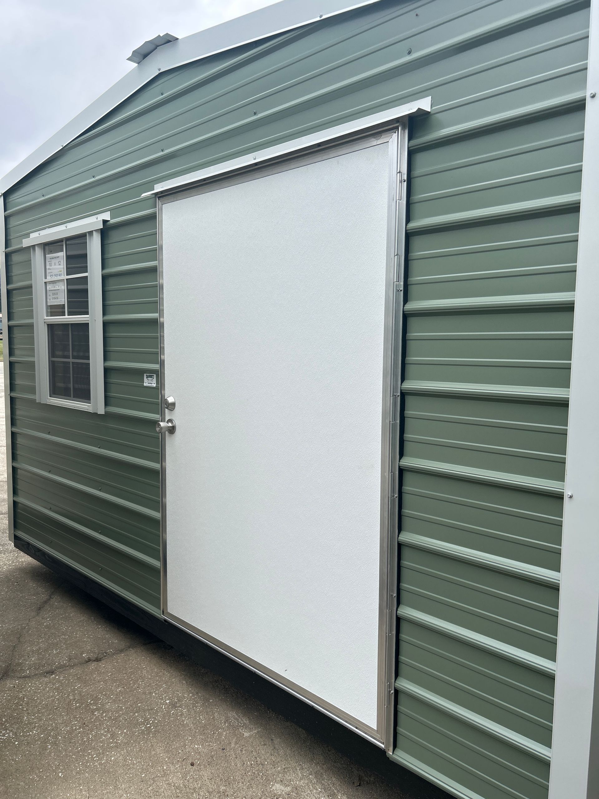 Green metal storage shed with a sliding white door and small window.