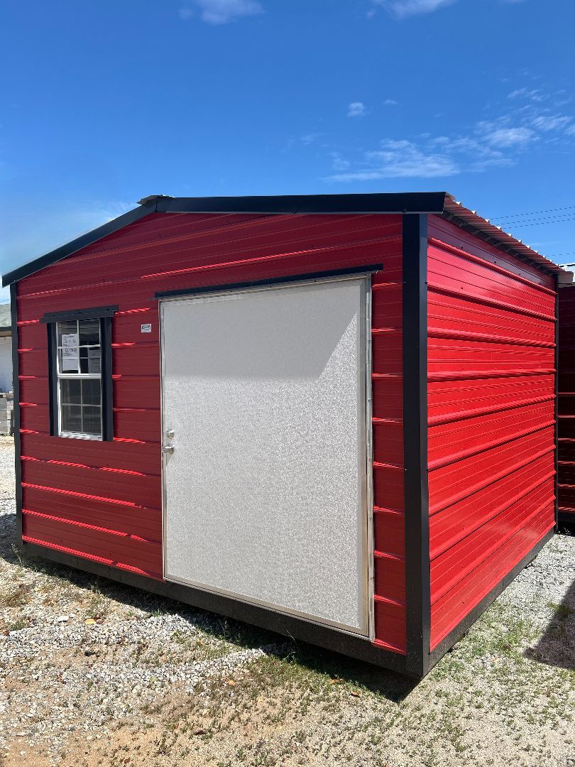 Red and black shed with a white door and small window against a blue sky.