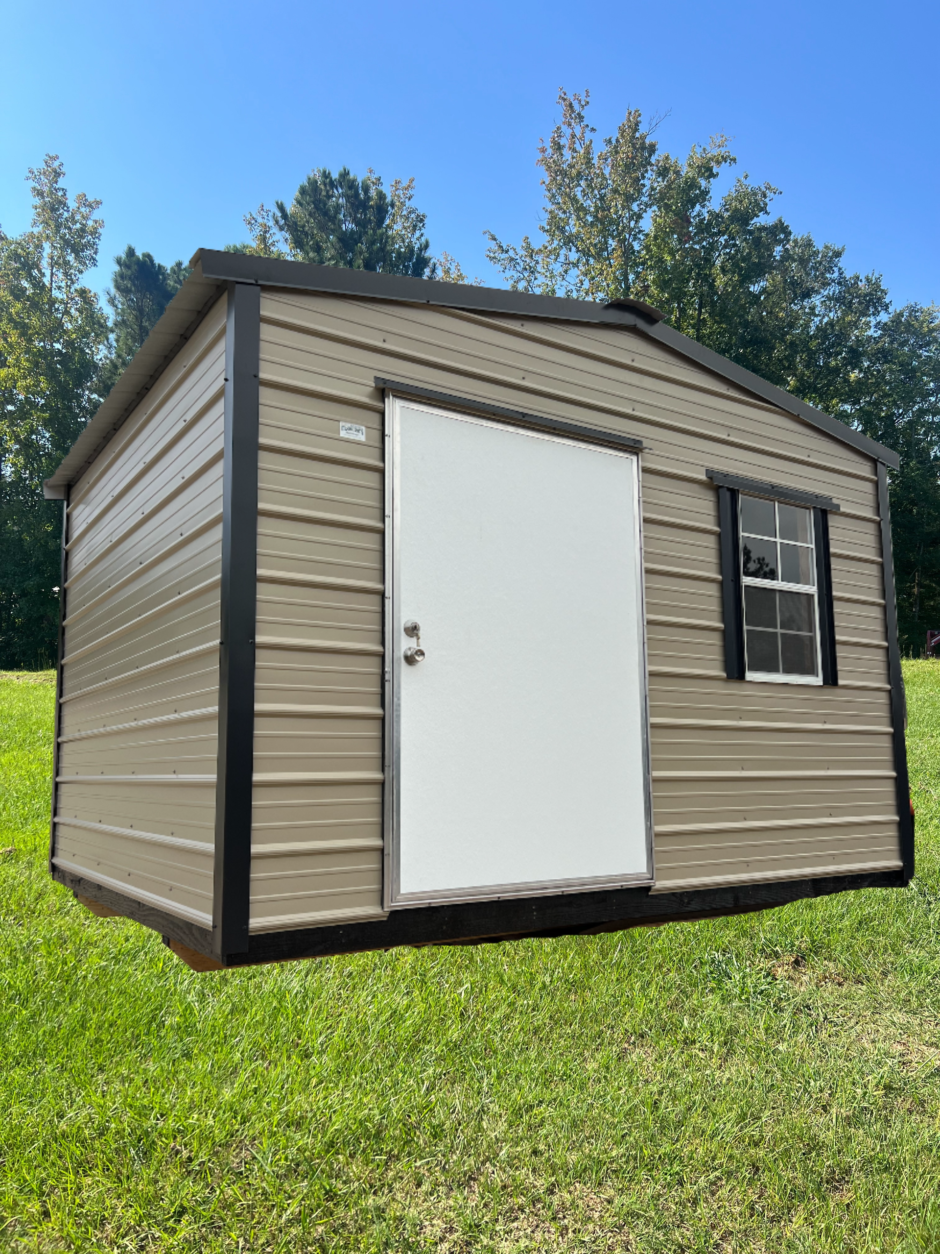 Tan shed with black trim, white door, and small window on a grassy lawn under a blue sky.